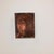 The artwork features an abstract representation of a face, rendered in deep, muted tones that evoke a sense of mystery and...