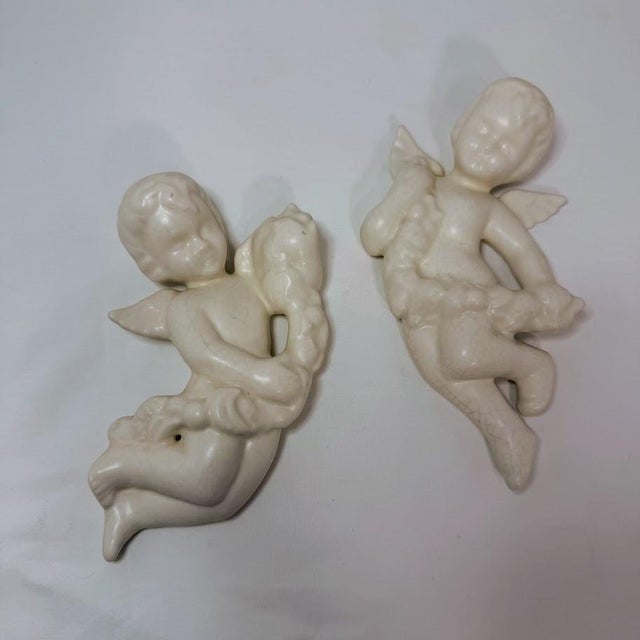 Vintage pair of ceramic cherub wall hangings by Cook, featuring a classic off-white or cream glaze with a beautiful aged...