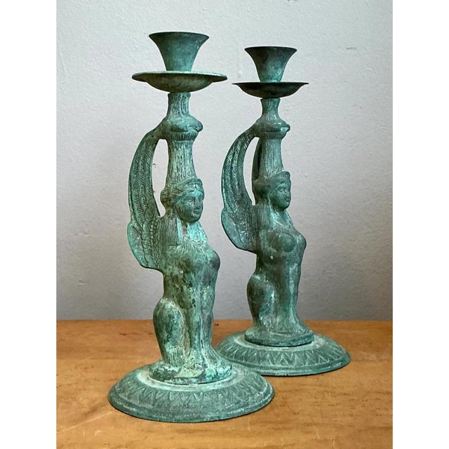 This captivating pair of vintage candleholders presents winged sphinx figures cast in bronze, each with a serene, softly...