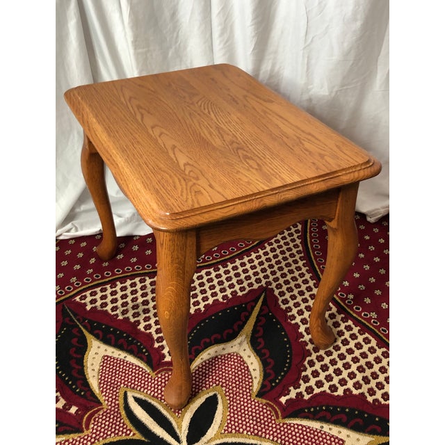 This vintage solid oak end table features a classic Late 20th-Century Colonial Revival silhouette with elegant Queen Anne-...