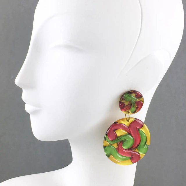 These stunning Lucite clip-on earrings feature a large disk-shaped dangling design with dimensional carving and multicolor...