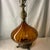 This is a vintage Hollywood Regency ribbed amber glass table lamp featuring an ornate cast brass footed base and neck.