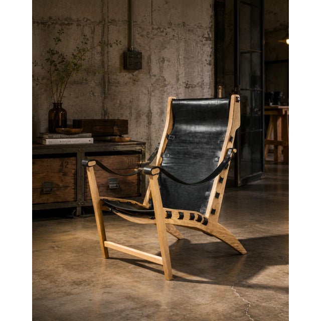Celtia pairs an exposed solid-wood frame with a black natural Galician leather sling that forms the seat and tall...