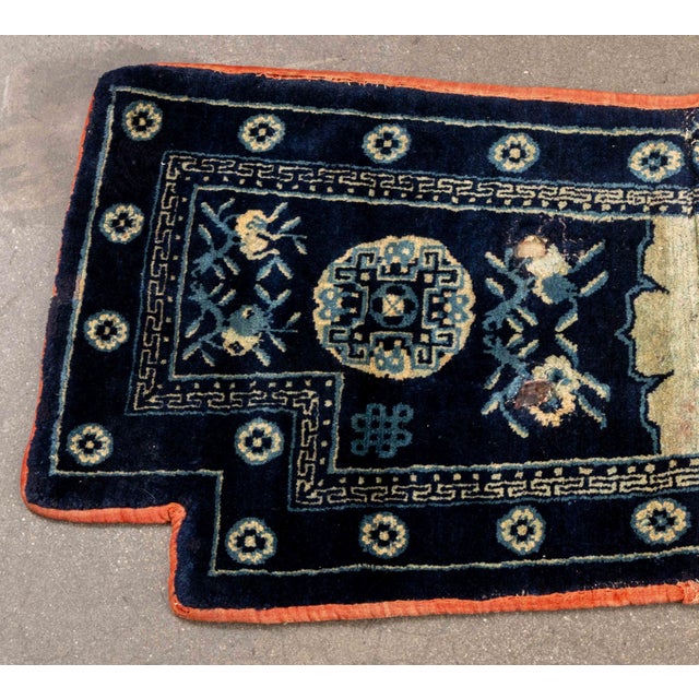 Chinese Pao Tao Blue Wool Saddle Rug, with floral and geometric designs and red trim. 4' 2" L x 2' W. Provenance: From a...