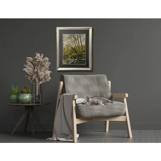 A tranquil French oil on board depicting a serene riverbank where tall trees rise gracefully and lean over the reflective...