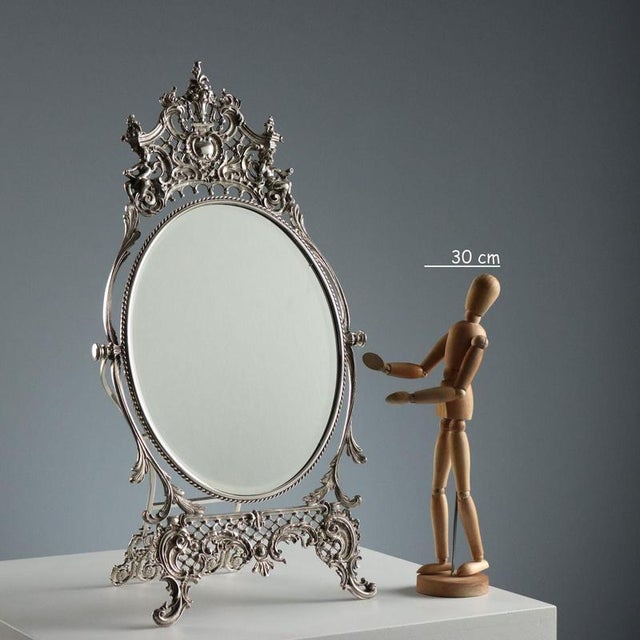 Table mirror with leafy scrollwork and cherub decorations. Oval beveled mirror. This piece is attributed to the mentioned...