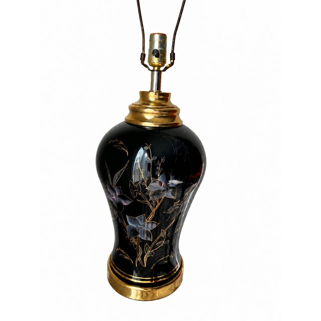 An elegant vintage table lamp featuring a glossy black vase-shaped body adorned with delicate gold-outline flowers,...