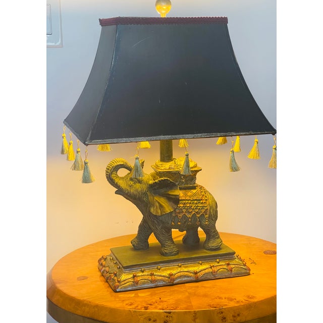 Sculptural elephant figure lamp with fringed lamp shade and gold tone accents.