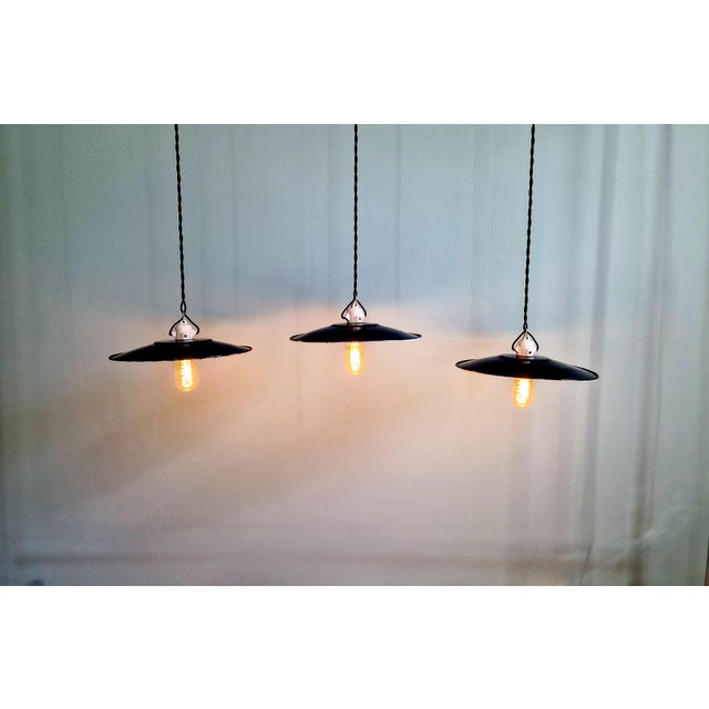 Trio of large industrial pendant lights in black enameled sheet metal from the mid-20th century. Each light has been...