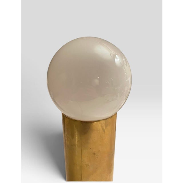 This lamp is a sleek brass cylinder column with a white bulb. Unsure of the designer. The cord looks to be from the 60s....
