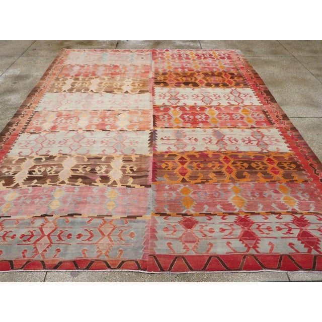 This mid-20th century Turkish Flatweave Kilim rug, showcases a bold and expressive design rich with traditional tribal...