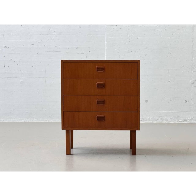 A compact mid-century modern chest of drawers in the clean, functional style of the 1960s, finished in warm teak veneer....