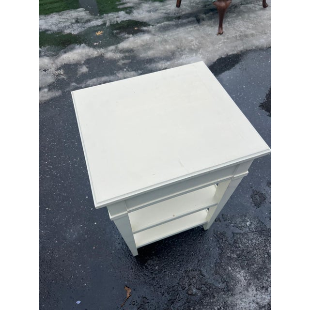 This charming white painted nightstand features clean, classic lines with a single drawer accented by a warm amber-tone...