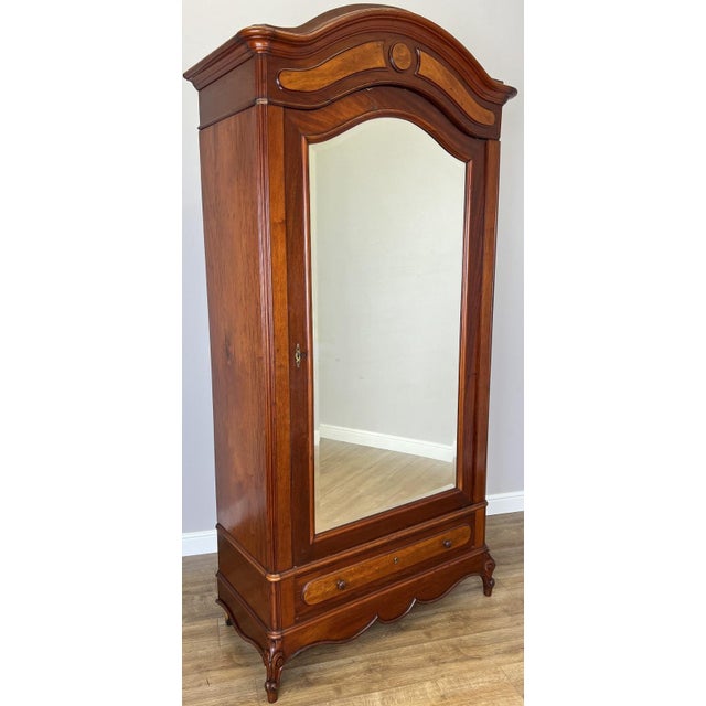 This elegant Antique French wardrobe features a beautifully shaped crown, a full-length polished mirror, and a rich...
