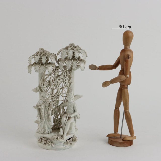 White earthenware group depicting a gallant scene. In the background, a pergola with palm trees and vines. This piece is...