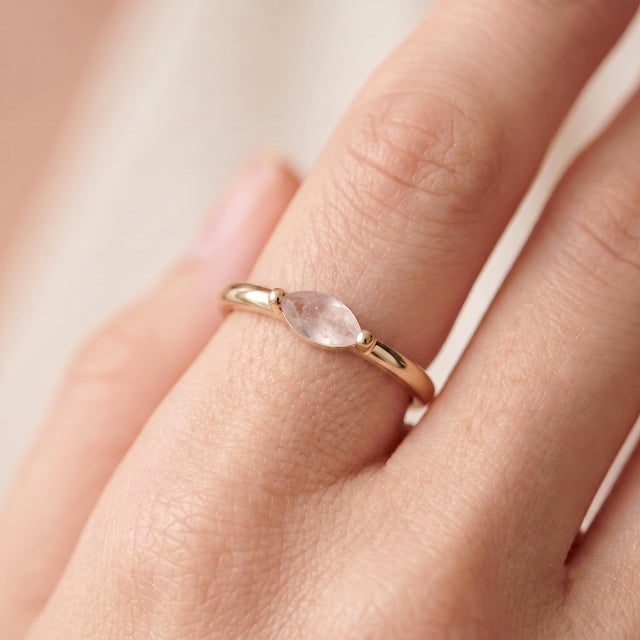 A soft, romantic solitaire featuring a blush pink marquise-cut rose quartz set in an east-west orientation, held by a...