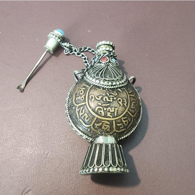 Tibetan-style decorative snuff bottle. Crafted from silver or white metal. The bottle has a footed bottom with a small...