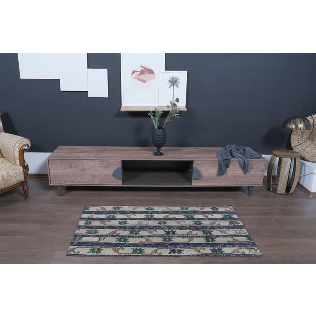 Patterns: Broad vertical navy blue stripes framed against a soft cream/beige base, featuring recurring green geometric...