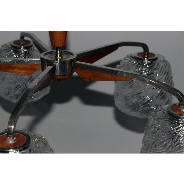 This five-light chandelier consists of a nickeled brass frame with teak details and cast glass shades. This piece is...