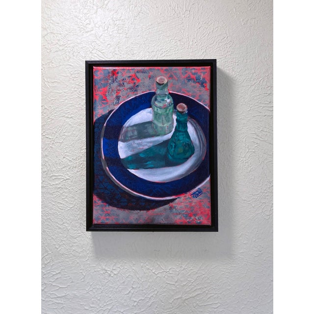 This oil on canvas piece depicts two vintage glass bottles resting on a decorative plate, their forms casting intriguing...