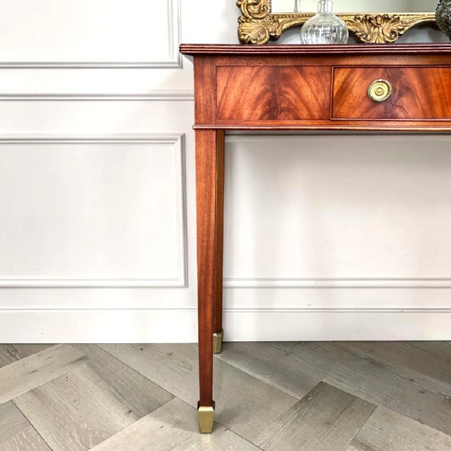 This Federal console table features luminous flame mahogany, a delicate satinwood inlaid top, elegant tapered legs, gold-...