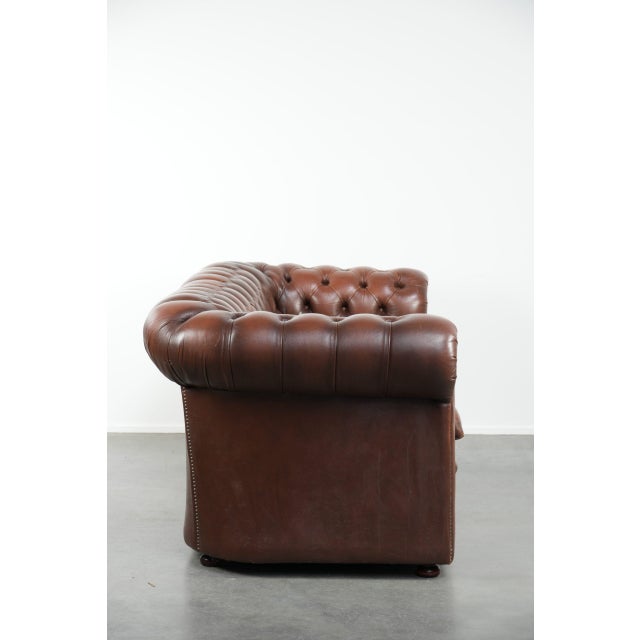 Vintage brown cowhide English Chesterfield 2.5-seater sofa with a rugged appearance. This brown Chesterfield sofa is made...