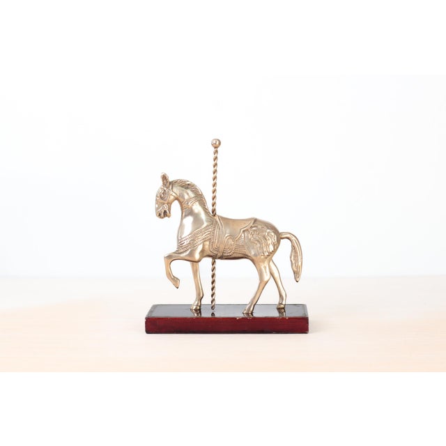 Vintage brass carousel horse figurine mounted on a polished wood base. Detailed saddle, twisted pole, and elegant prancing...