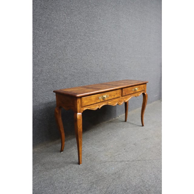 Henredon console table in oak with two drawers and a plank-style top. Features a scalloped apron and curved legs with...