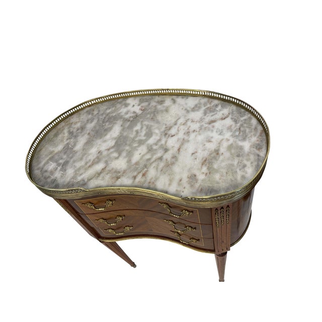 An elegant pair of matching Louis XVI style kidney-shaped bouillote tables with marble tops surrounded by pierced brass...