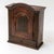 A rustic softwood hanging cupboard with a dark finish. The piece features a curved, arched top and fluted side panels. The...