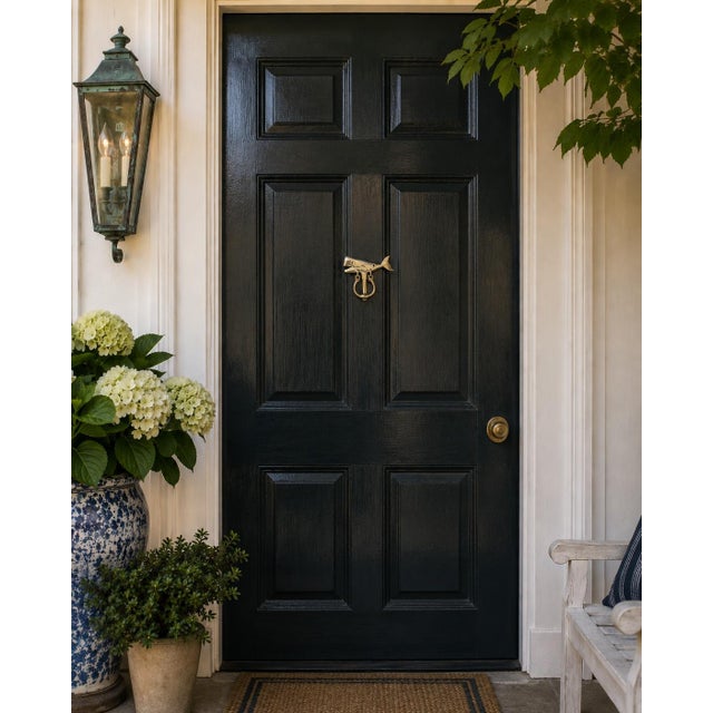 A distinctive vintage door knocker cast in brass in the form of a stylized whale, complete with a broad tail, open mouth,...