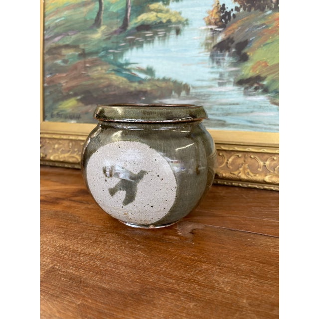 This vintage studio pottery jar features a rounded, bulbous form with a rich olive green glaze and a striking bird...