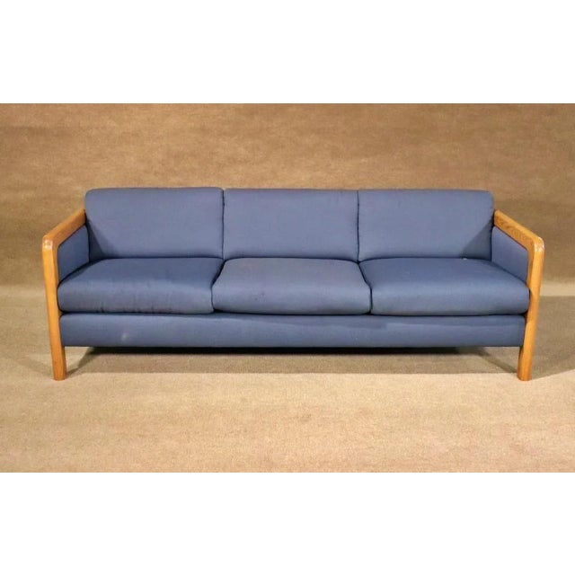 This attractive vintage modern sofa boasts a single overstuffed cushion covered in a plush royal blue upholstery. The...