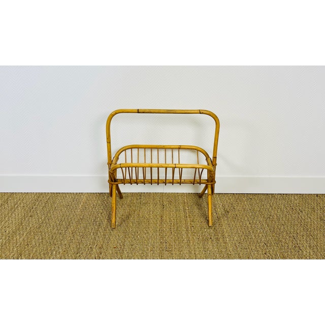 A charming rattan magazine rack dating from the 1960s. it rests on four crossed legs and has an integrated handle. the...