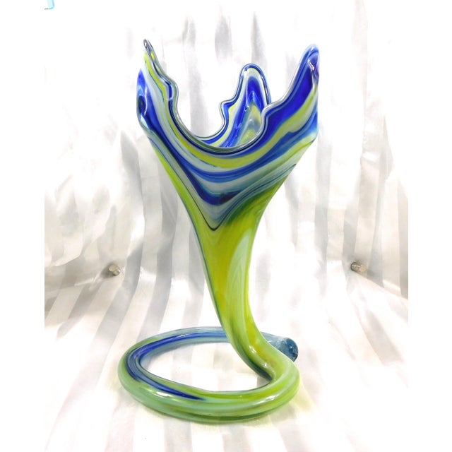 This is a blue and yellow, andmaybe white, art glas vase. The vase is triangular is shape with three tall point at the...