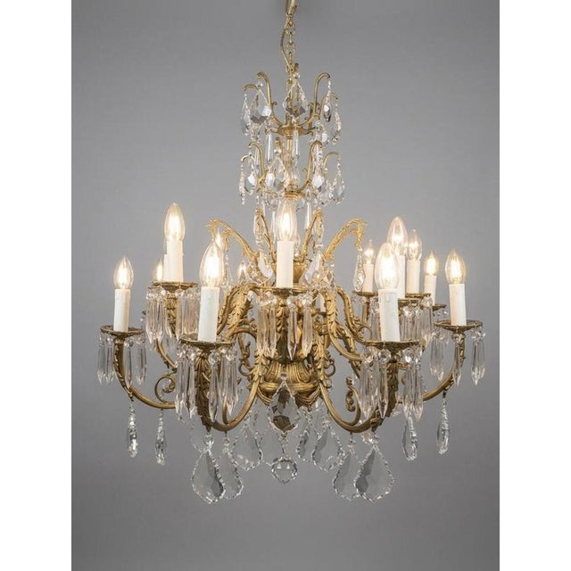 An impressive French brass and crystal chandelier featuring 16 light points and an elegant symmetrical design richly...