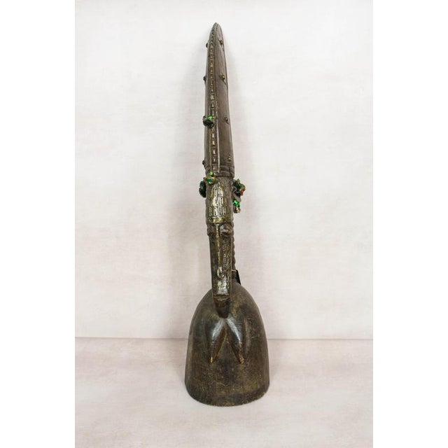 A hand-carved helmet mask from mali, embellished with metal and fabric detail. Each mask represents either a male or...