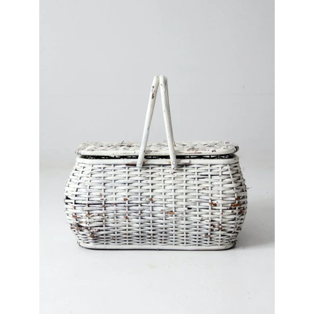 Vintage white wicker basket featuring a large woven form with a hinged lid and double handles. The airy construction and...