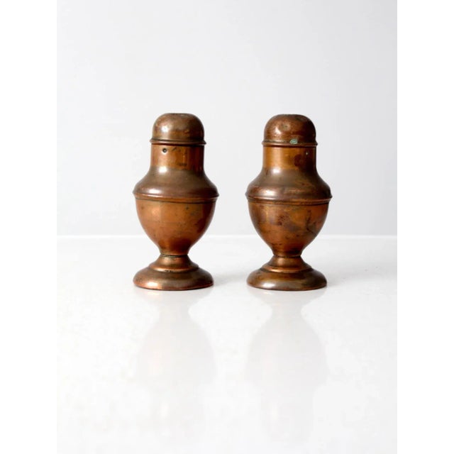 A vintage set of copper salt and pepper shakers, gracefully aged with a warm patina that highlights their hand-crafted...