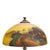 This antique table lamp features a reverse-painted glass shade depicting a scenic landscape, characteristic of the early...
