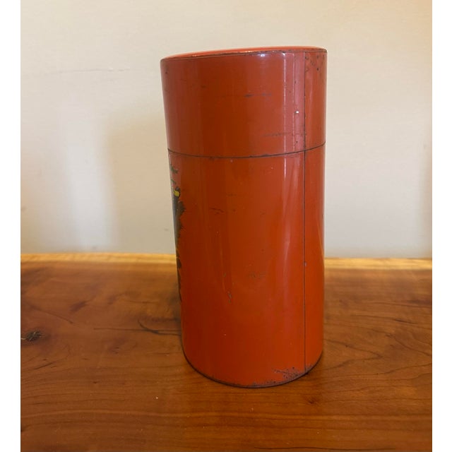 A striking vintage Japanese tea canister featuring a vivid red lacquer finish adorned with a hand-painted landscape of...
