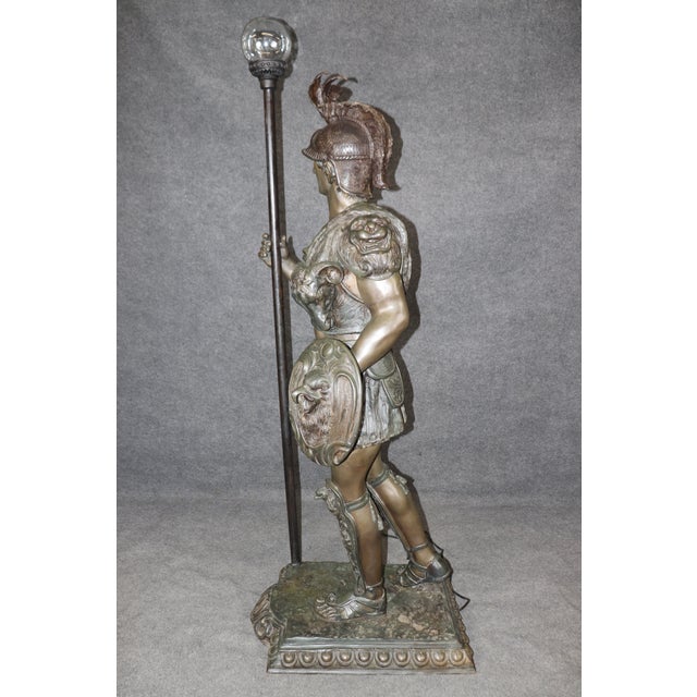 This life-size cast bronze Roman Centurion soldier torchiere floor lamp, circa 1920, is a commanding work of decorative...