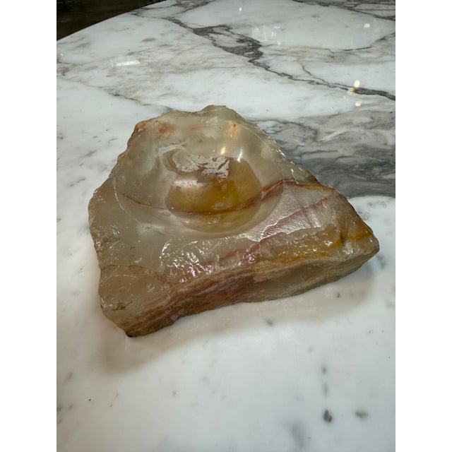 Solid natural marble ashtray featuring creamy translucent tones with honey-gold and reddish-brown veining. Its polished...