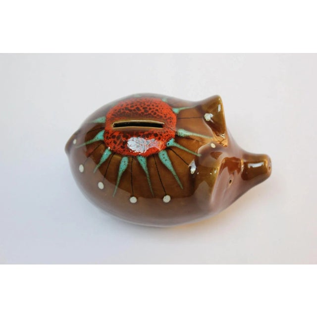 Ceramic piggy bank by Bertoncello featuring a drip glaze decoration in orange, white and green against a high-gloss brown...