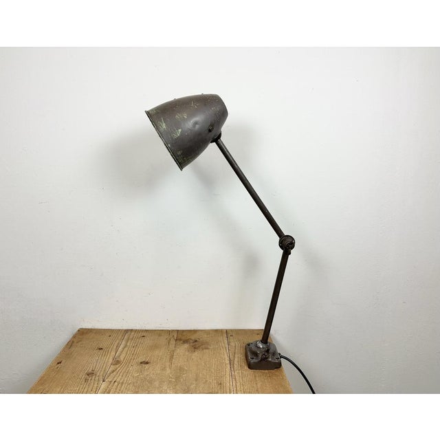 This brown industrial desk lamp was made in former Czechoslovakia during the 1960s. It features an iron body with three...