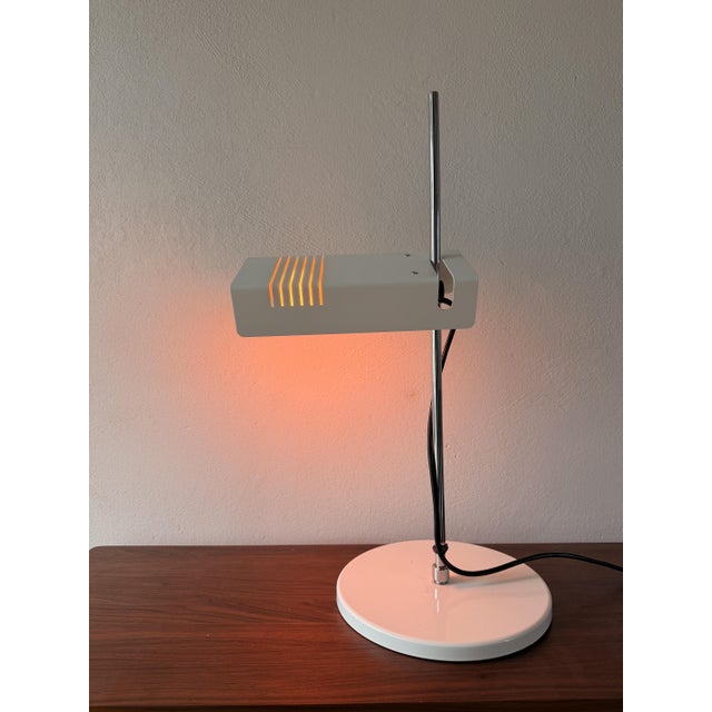 A distinctive space-age desk lamp, likely from the 1970s. It features a rectangular, slotted metal shade, a slender chrome...