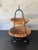 Vintage mid-century two-tier basket featuring handwoven rattan and cane baskets supported by a sculptural black iron...