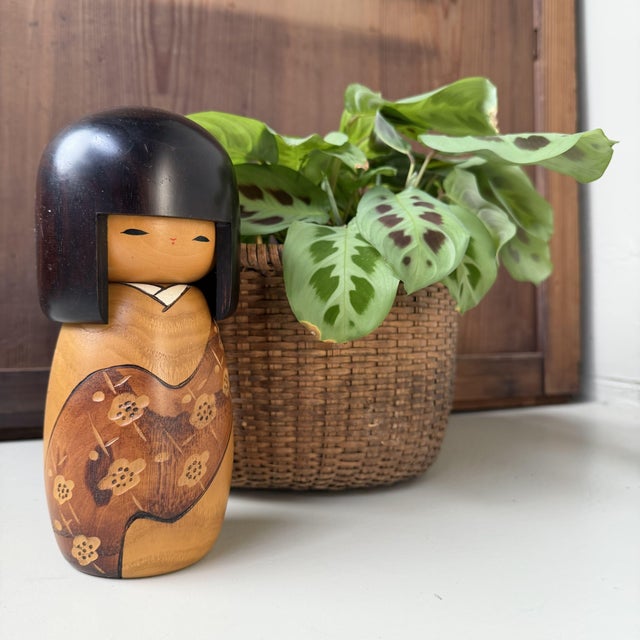 This vintage Japanese kokeshi by Usaburo has a soft, rounded form with a large dark hairstyle and a calm, understated...