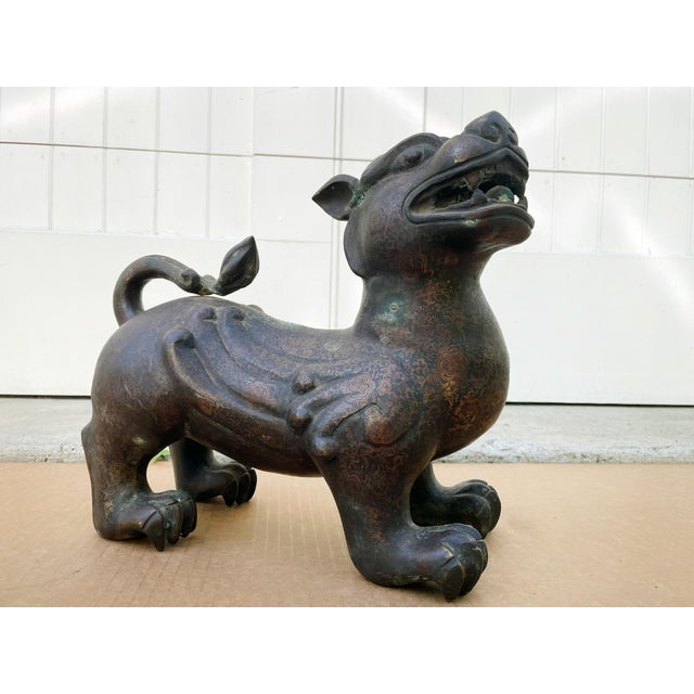 This bronze guardian lion or foo dog was crafted in the 20th Century and rendered with an intricate floral-patterned...