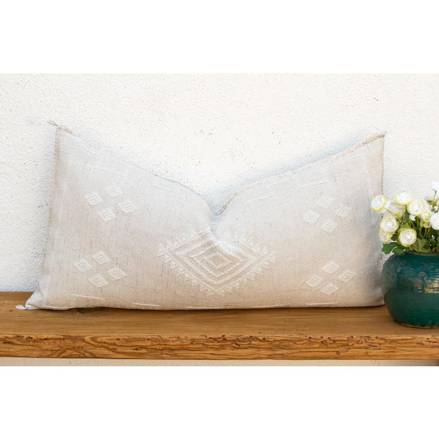 This handcrafted Moroccan cactus silk lumbar pillow reads first as texture, then as pattern — a soft tonal ivory ground...
